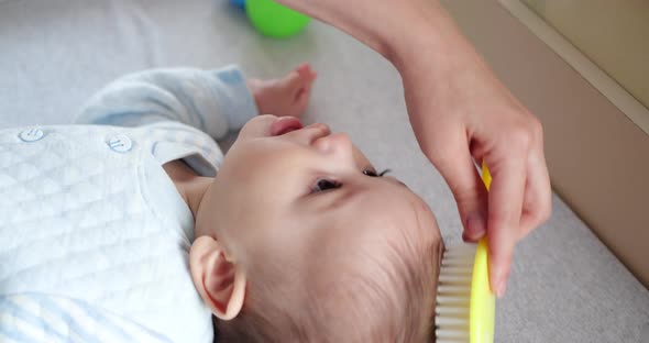 Mother Combing Tiny Hairs on Her Newborn Baby's Head As She Wakes Up alt