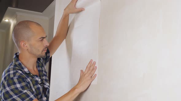 A Man Tries on Several Pieces of Wallpaper on the Wall Choosing the Appropriate One