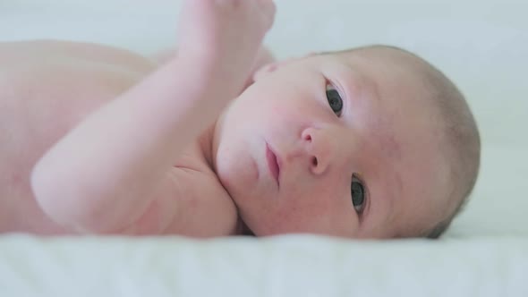 Naked newborn baby lies in a white crib, face close-up