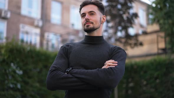 Medium Shot of Confident Stylish Man with Crossed Hands Looking Away Standing on City Street alt