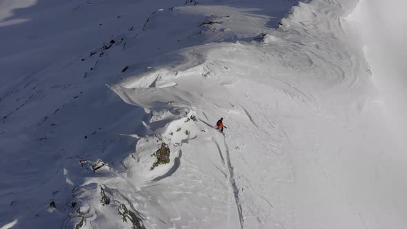 Drone follow shot of snowboarder gliding over dangerous ridge to get to drop in spot alt