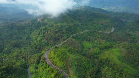 Aerial view over a winding road in the mountains of a tropical forest, Thailand. alt