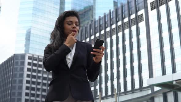 Slow motion of thoughtful smiling young Indian businesswoman looking at mobile phone