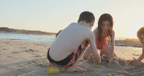 Three kids playing on the beach building sand castles together alt