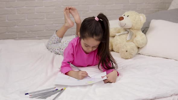 Cute Little Girl Drawing Pictures While Lying on Bed