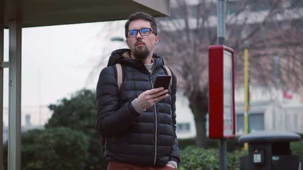 Citizen Waits for Bus at Stop Holding Smartphone alt