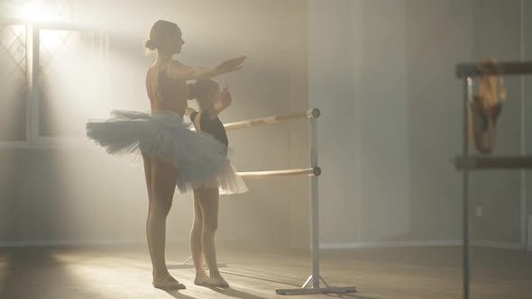 Caucasian Ballet Teacher Explaining Hands Movement to Talented Girl in Dancing Studio in Backlit Fog alt