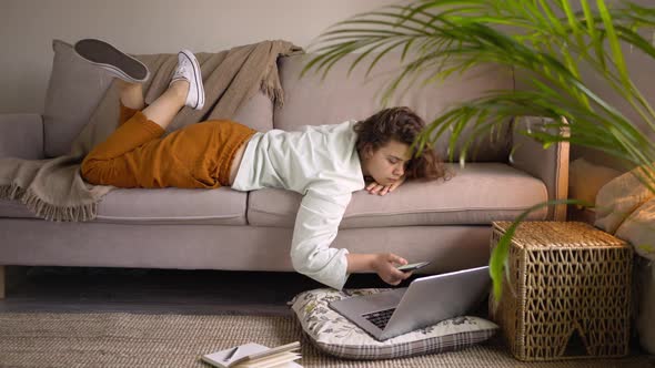 Freelancer with Curly Hair Lies on Sofa Typing on Smartphone