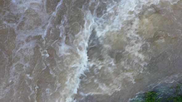 Fast flowing turbulent water with a brown coloration and white foam alt