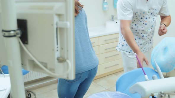 A young girl enters the office of a dental clinic and sits in the dentist chair. alt