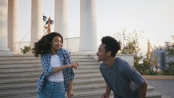Ethnic Black Friends Smiling and Dancing Against Pillared Observation Deck in Park alt