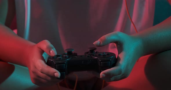 Close-up of women's hands with a game console controller while playing. Colorful lights alt