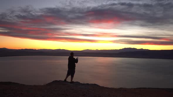 Person on viewpoint taking panoramic photo of vibrant sunset overlooking lake alt