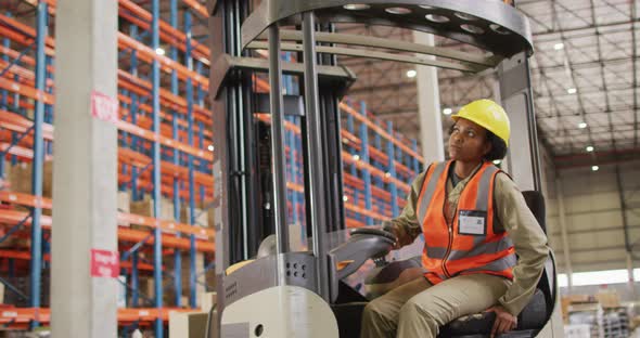 African american female worker wearing safety suit and sitting in turret truck in warehouse alt