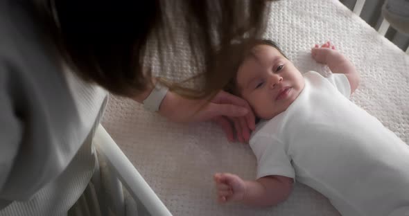 Loving Mom Strokes a Newborn Baby Lying on Its Back in a Child Crib alt