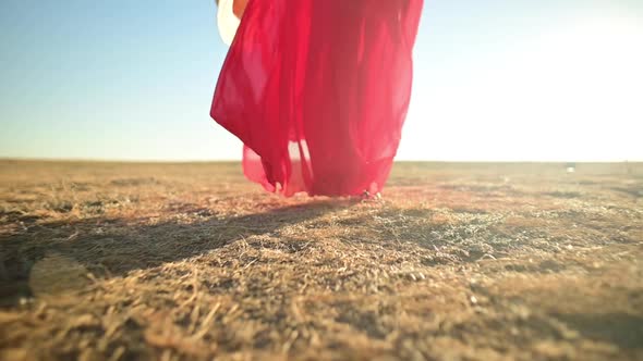 Closeup Female Slender Legs in Sandals in a Red Loose Transparent Dress That Flutters in the Wind in alt