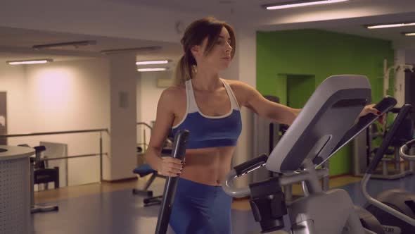 Slim Girl with Shapely Brawny Body Using Elliptical Trainers for Warm Up alt