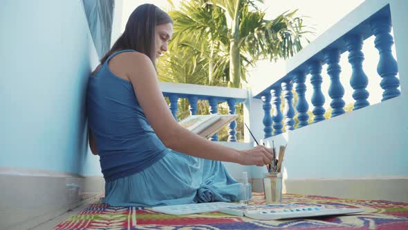 Young female artist painting a pineapple by watercolors