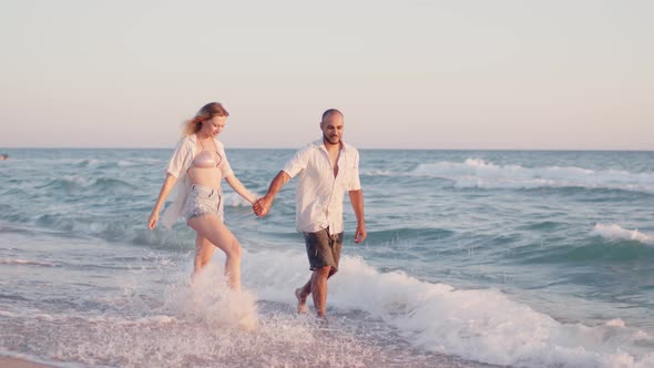 Couple of Young Lovers Holding Hands Walking Along the Beach By the Sea