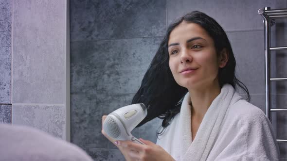 Beautiful Caucasian Woman Looking at Her Reflection in the Mirror and Smiling While Drying Hair with
