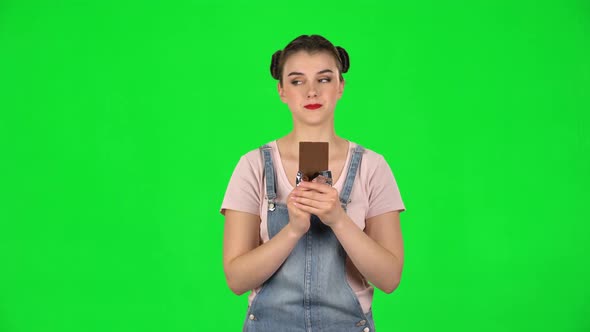 Girl with Great Pleasure Eats Chocolate on a Green Screen in the Studio alt