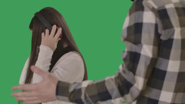 Teenage Girl Showing Tongue To Unrecognizable Father Gesturing. Caucasian Daughter in Headphones alt