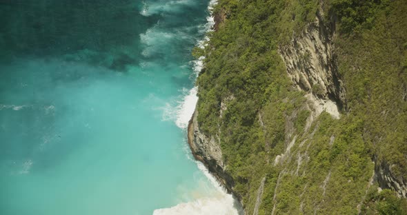 Close Up Slow Motion Shot of Blue Waves Crashing on the Rocky Cliffs with Tropical Vegetation Above alt