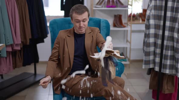 Joyful Confident Gay Man Popping Champagne Sitting in Clothing Shop Indoors Laughing Out Loud alt