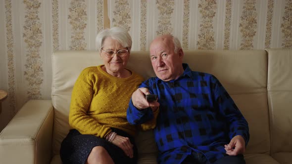Middle Aged Caucasian Couple Watching Tv Using Remote Control Looking at the Camera and Laughing alt