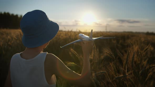Funny Boy Playing with Airplane in Golden Wheat Field at Sunset