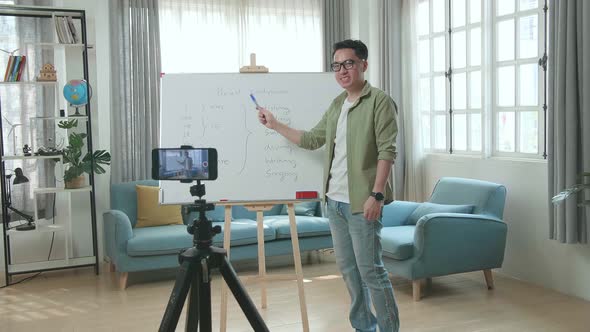 Asian Male Teacher With Glasses Shoots Video By Smartphone Camera While Teaching English At Home alt