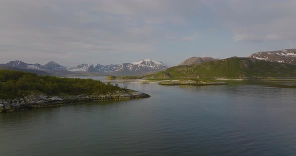 Aerial push in towards lush islands, seagulls fly past, Sommaroya Bridge and mountains in background alt