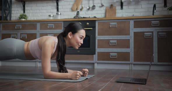 Healthy Asian Yoga Woman Standing in Plank with Online Trainer Using Laptop alt