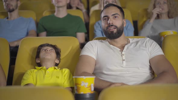 Cheerful Middle Eastern Man and Boy Watching Film in Cinema and Talking. Portrait of Happy Father alt