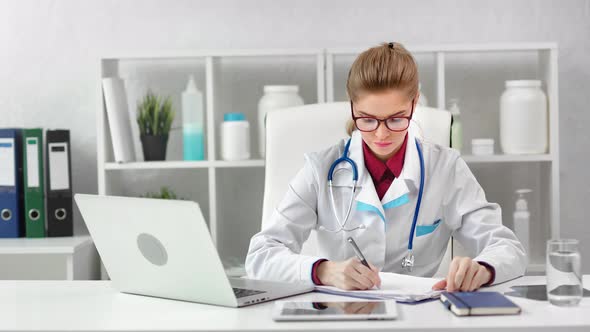 Enthusiastic Young Female Medical Worker Looking at Screen of Laptop Pc Taking Note alt