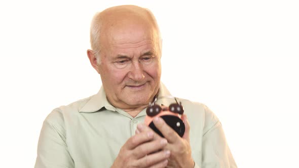 Old Man Looking at an Alarm Clock Smiling To the Camera alt