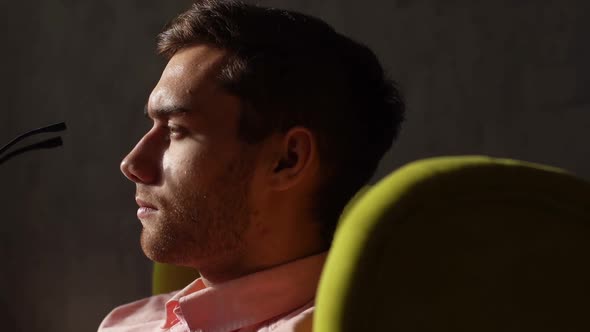 Closeup Face of Handsome Young Man Putting Glasses on Face Sitting in Yellow Chair on Black Isolated alt