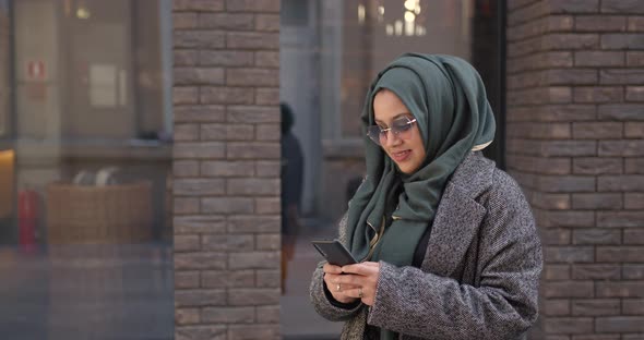 Muslim Woman Using Her Phone Standing Near Building alt