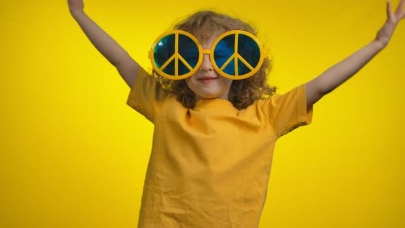 Curly Little Girl in Yellow Hippie Sunglasses is Dancing on a Yellow Background alt