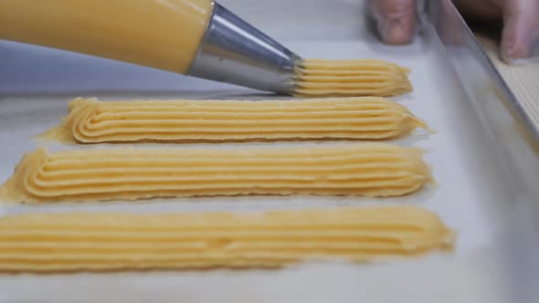 The Pastry Chef Applies the Dough for the Eclair to the Paper in a Baking Sheet alt