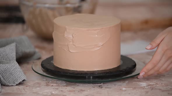 Pastry Chef Woman Is Smearing Chocolate Cream On Sponge Cake With Spatula On Rotating Cake.