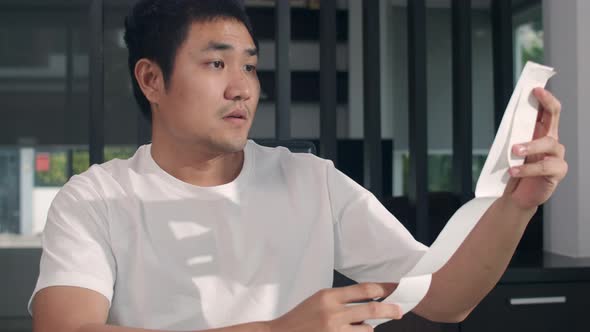 Young Asian business man records of income and expenses at home. male worried, serious, stress