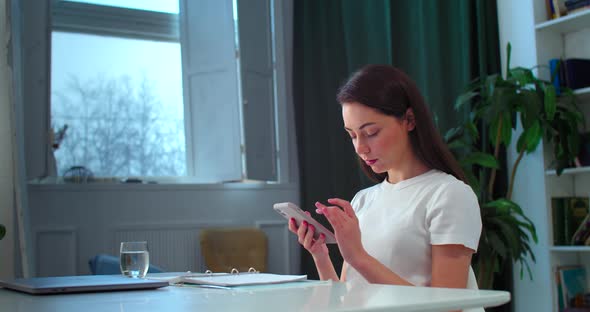 Serious Girl Holding Smartphone While Studying at Home Interior Background
