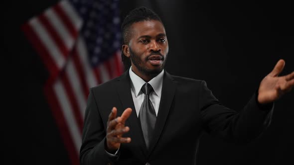 Persuasive Confident African American Man Talking and Gesturing with Blurred US Flag at Black alt