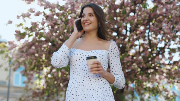 Cheerful Woman Relaxing with Cellphone and Hot Drink Outdoors