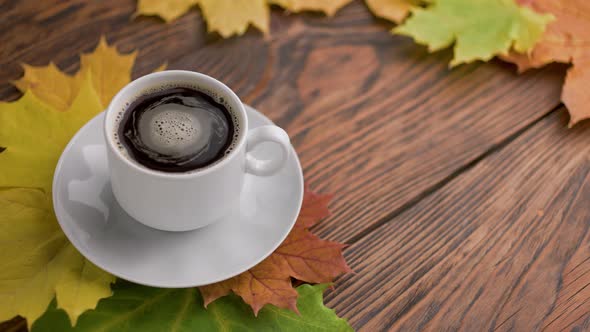 Coffe Cup on Wooden Table with Colorful Autumnal Maple Leaves with Spinning Coffee Bubbles