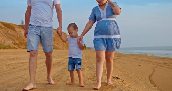 Cheerful Kid Walks Along the Seashore with Mother and Father Walks Barefoot on the Sand