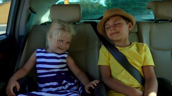 Little Beautiful Boy in Hat and Blond Girl are Riding in the Backseat of the Car alt