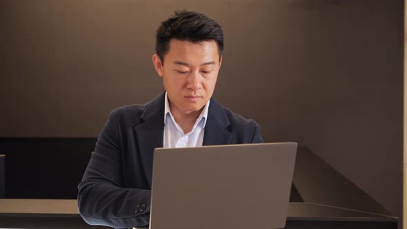 Asian Male Executive Typing Work Email on Computer Laptop in Lobby Place alt