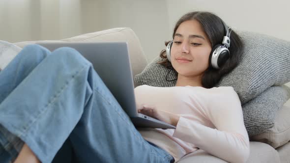 Relaxed Arabian Woman Freelancer Female Student Browsing Networks Lying on Sofa Looks at Laptop alt